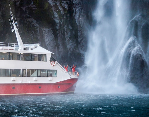 Cruise ship near waterfall in Milford Sound, New Zealand, with passengers on deck.