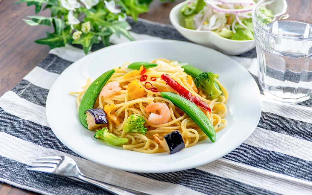Prawn Aglio Olio with vegetables on a white plate, served on a striped cloth.