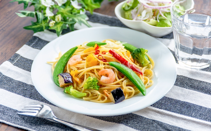 Prawn Aglio Olio with vegetables on a white plate, served on a striped cloth.