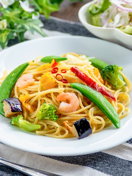 Prawn Aglio Olio with vegetables on a white plate, served on a striped cloth.