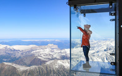 Person in glass box overlooking snowy Alps on Chamonix Mont Blanc day trip.
