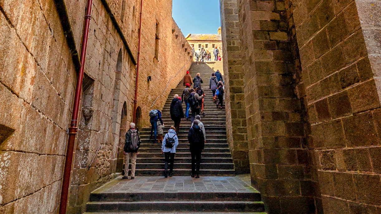 Tourists walking on cobblestone streets exploring Mont Saint Michel, France.