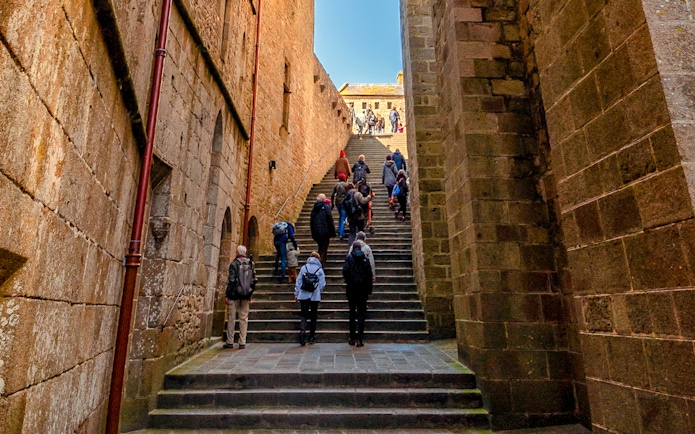Tourists ascending stone steps in Mont Saint Michel, France.