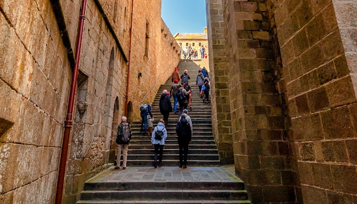 Tourists walking on cobblestone streets exploring Mont Saint Michel, France.