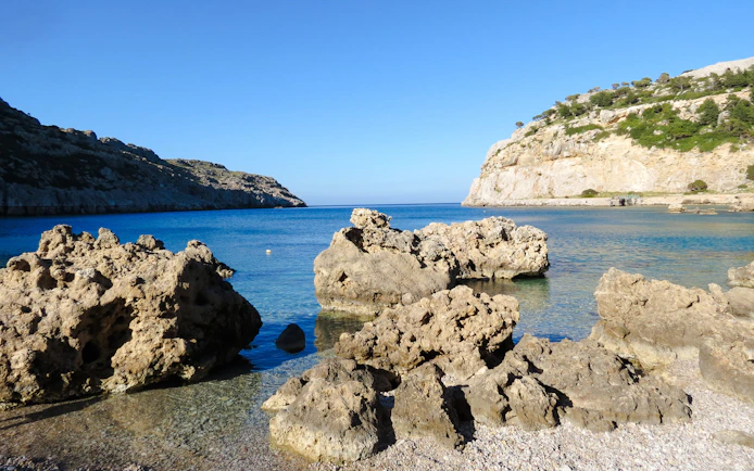Rocky shoreline of Navarone Bay with clear blue water, Island of Rhodes, Greece.