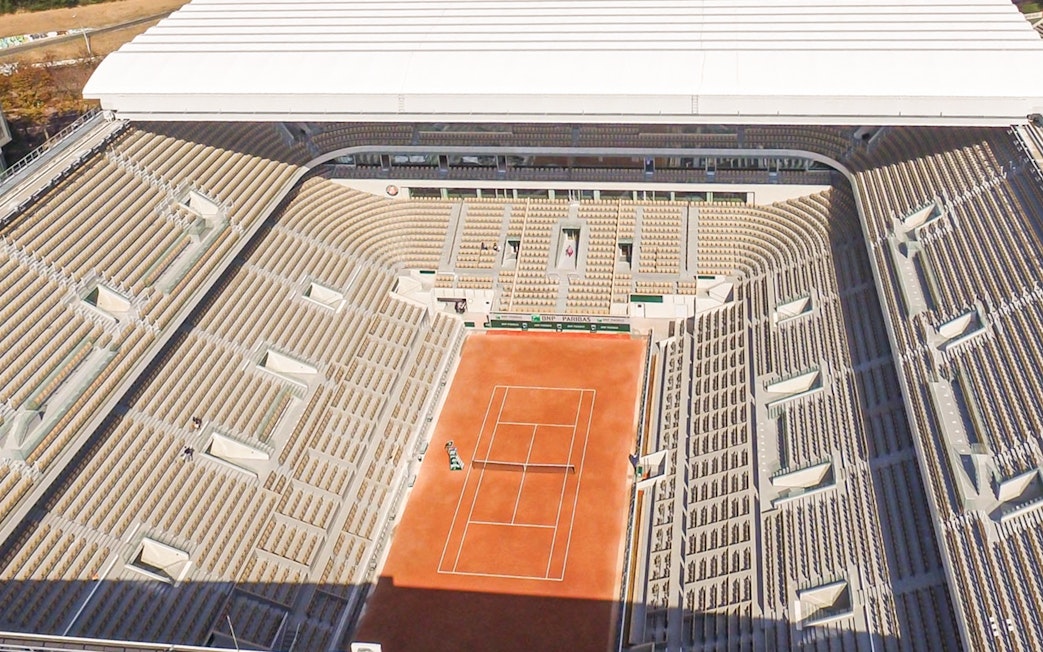 Roland Garros Stadium interior with clay tennis court and surrounding seating area.