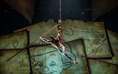 Performer suspended in air during "Drawn to Life" show with animated backdrop.