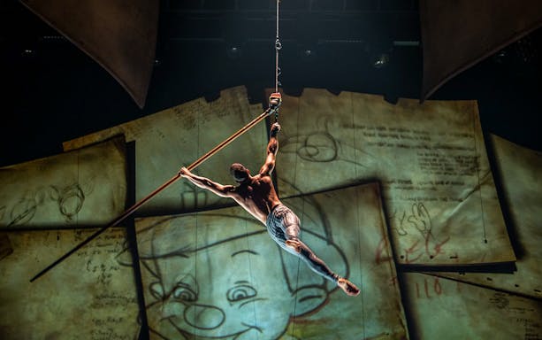 Performer suspended in air during "Drawn to Life" show with animated backdrop.