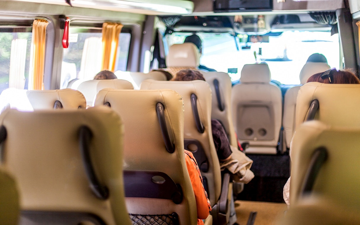 Minivan interior with beige seats and passengers seated, view towards the front.
