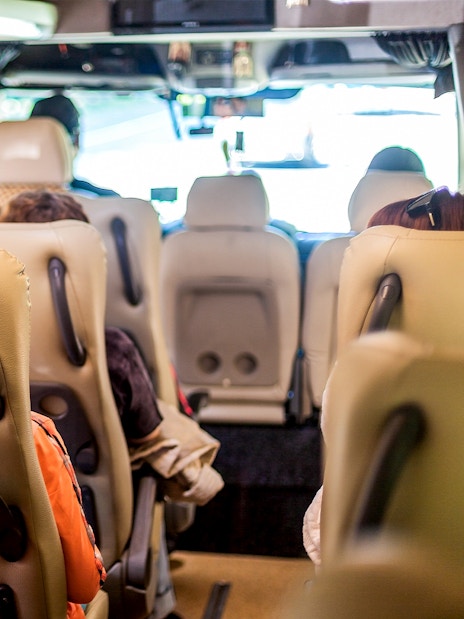 Minivan interior with beige seats and passengers seated, view towards the front.