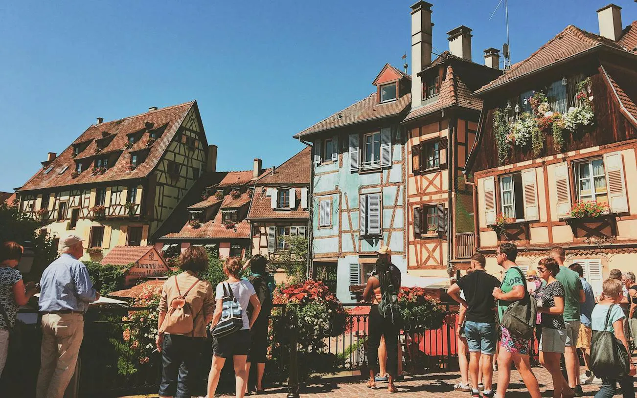 Tourists exploring half-timbered medieval buildings in Colmar, France.