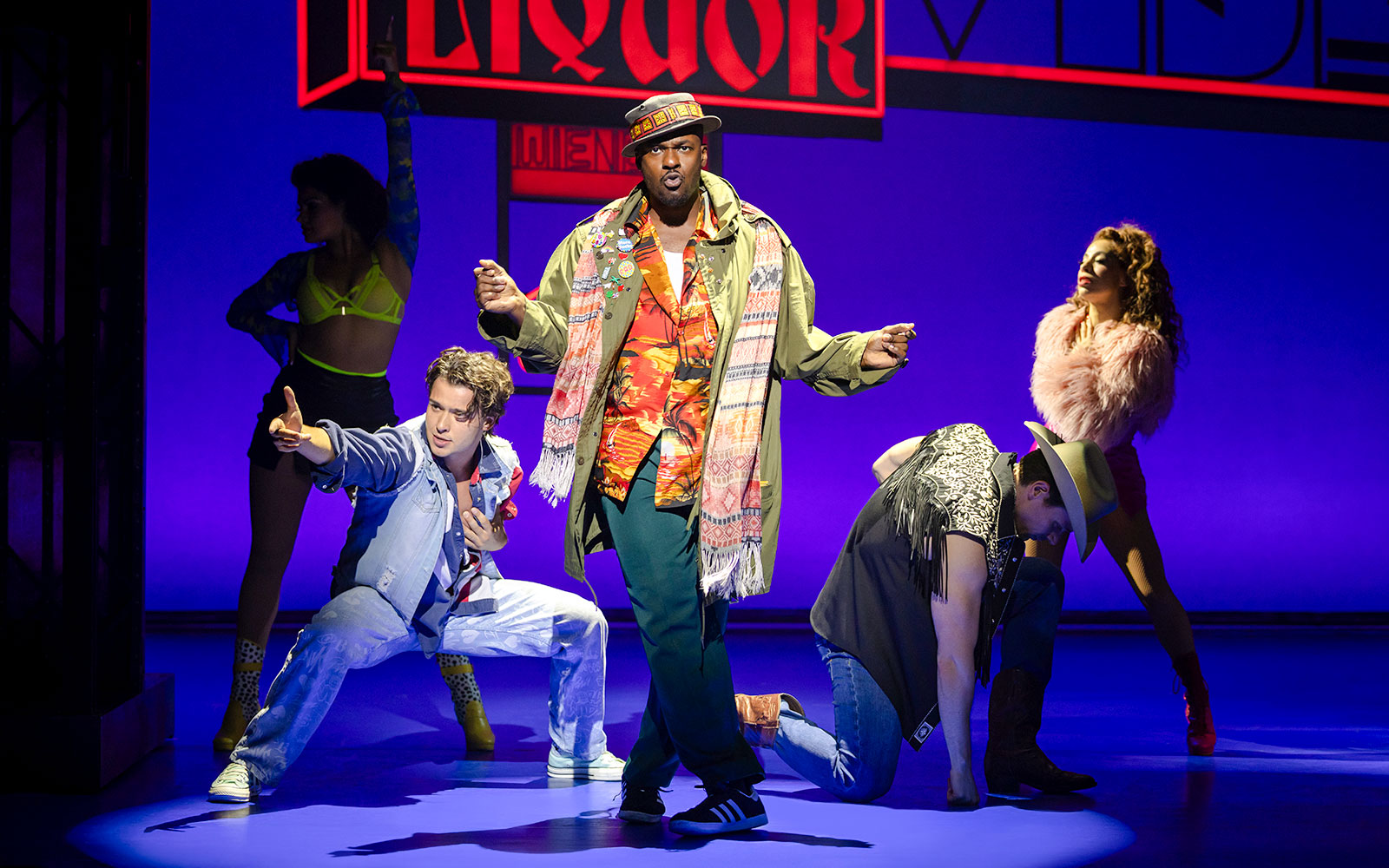Cast performing a lively scene from Pretty Woman The Musical with colorful neon signs.