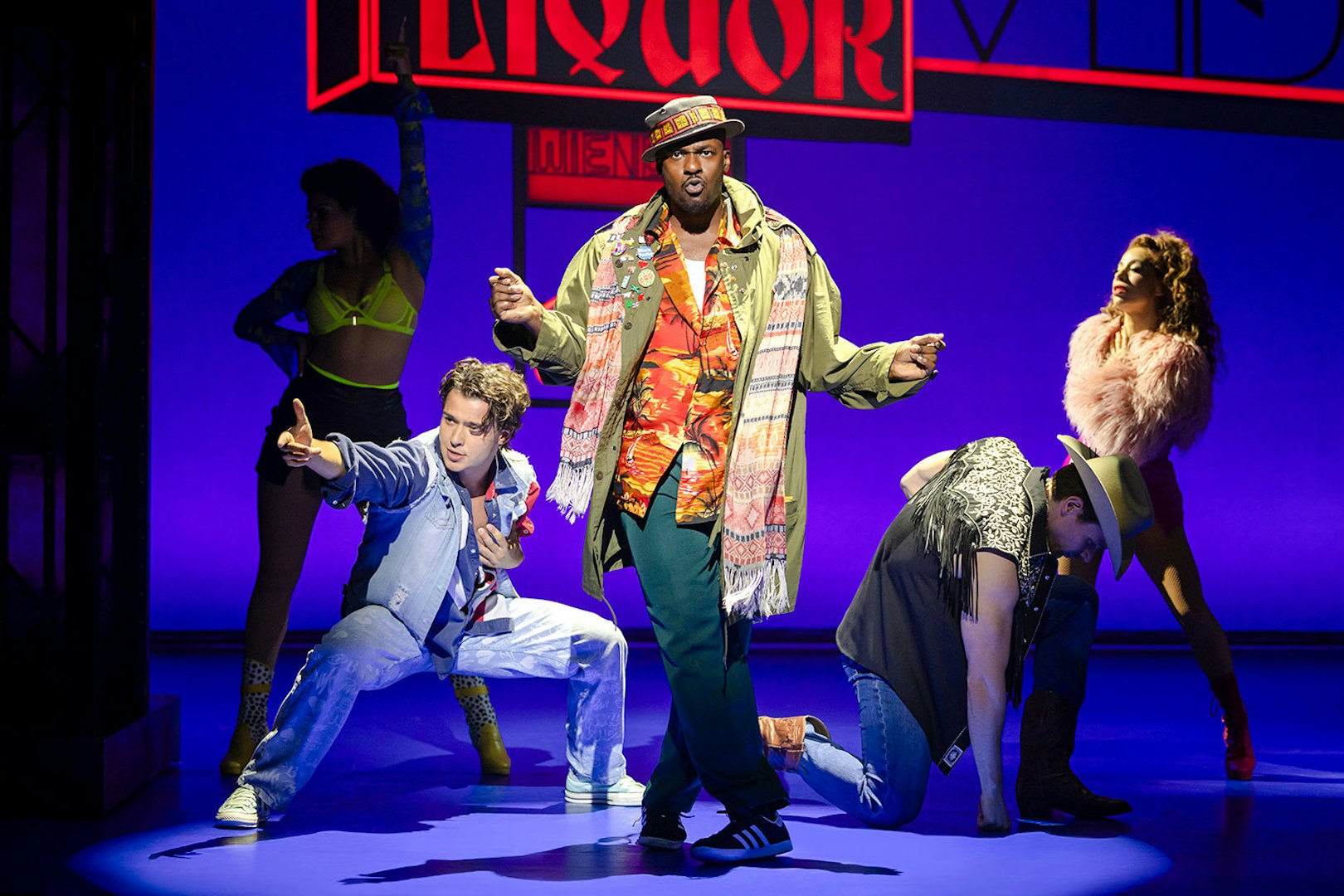 Cast performing a lively scene from Pretty Woman The Musical with colorful neon signs.