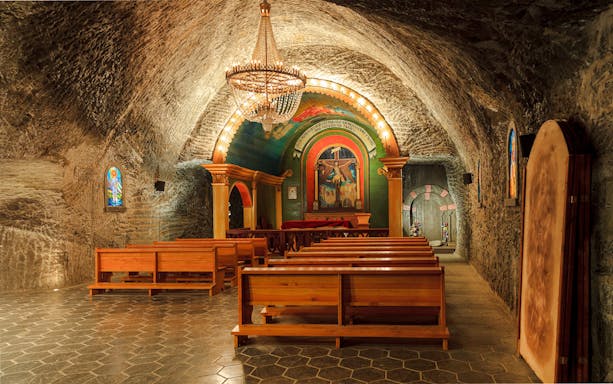 St John Chapel interior in Wieliczka Salt Mine with wooden benches and ornate altar.