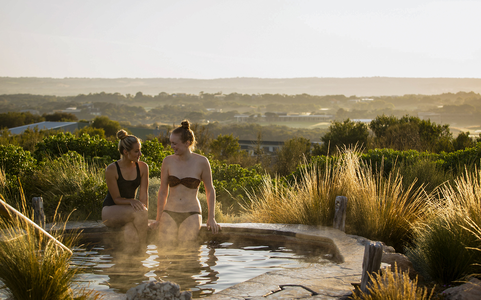 Two people relaxing in a hot spring at Peninsula Hot Springs with scenic views.