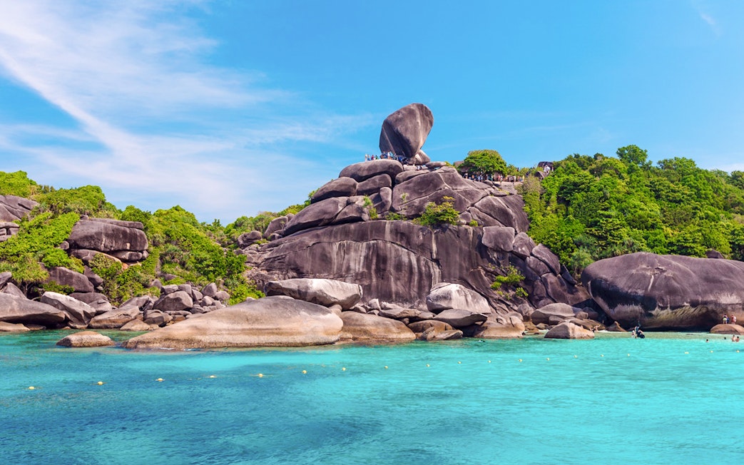 View of Similan Island's rocky shoreline and clear blue water from a boat.