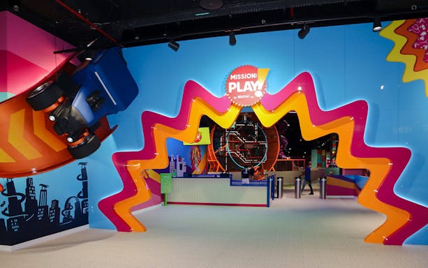 Entrance to Mission: Play! by Mattel with colorful zigzag design and suspended car display.
