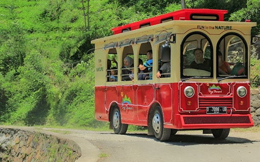 Red tram at Dago Dreampark, Bandung, carrying visitors through lush greenery.