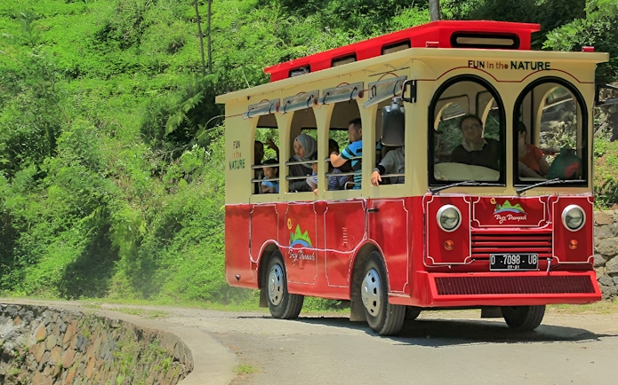 Red tram at Dago Dreampark, Bandung, carrying visitors through lush greenery.