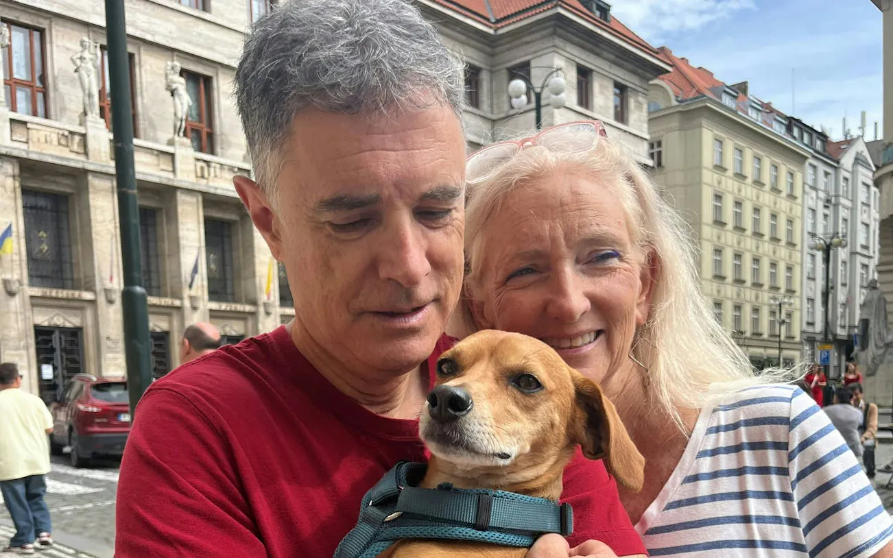 Couple with a dog in front of historic Prague architecture during city exploration game.