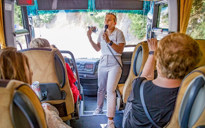 Tour guide speaking to passengers on a bus during the Meteora Monasteries tour from Athens.