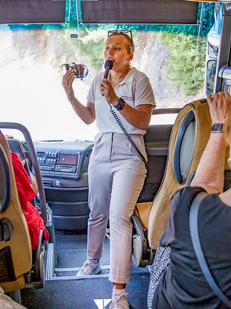Tour guide speaking to passengers on a bus during the Meteora Monasteries tour from Athens.