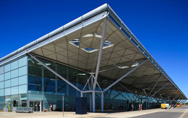 Stansted Airport terminal exterior with buses and travelers.