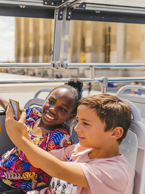 Children on a double-decker bus enjoying an audio-guided tour with the Eiffel Tower in the background.