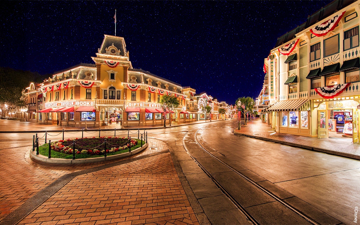 Main Street USA at night, Disneyland Park California, with illuminated shops and decorations.