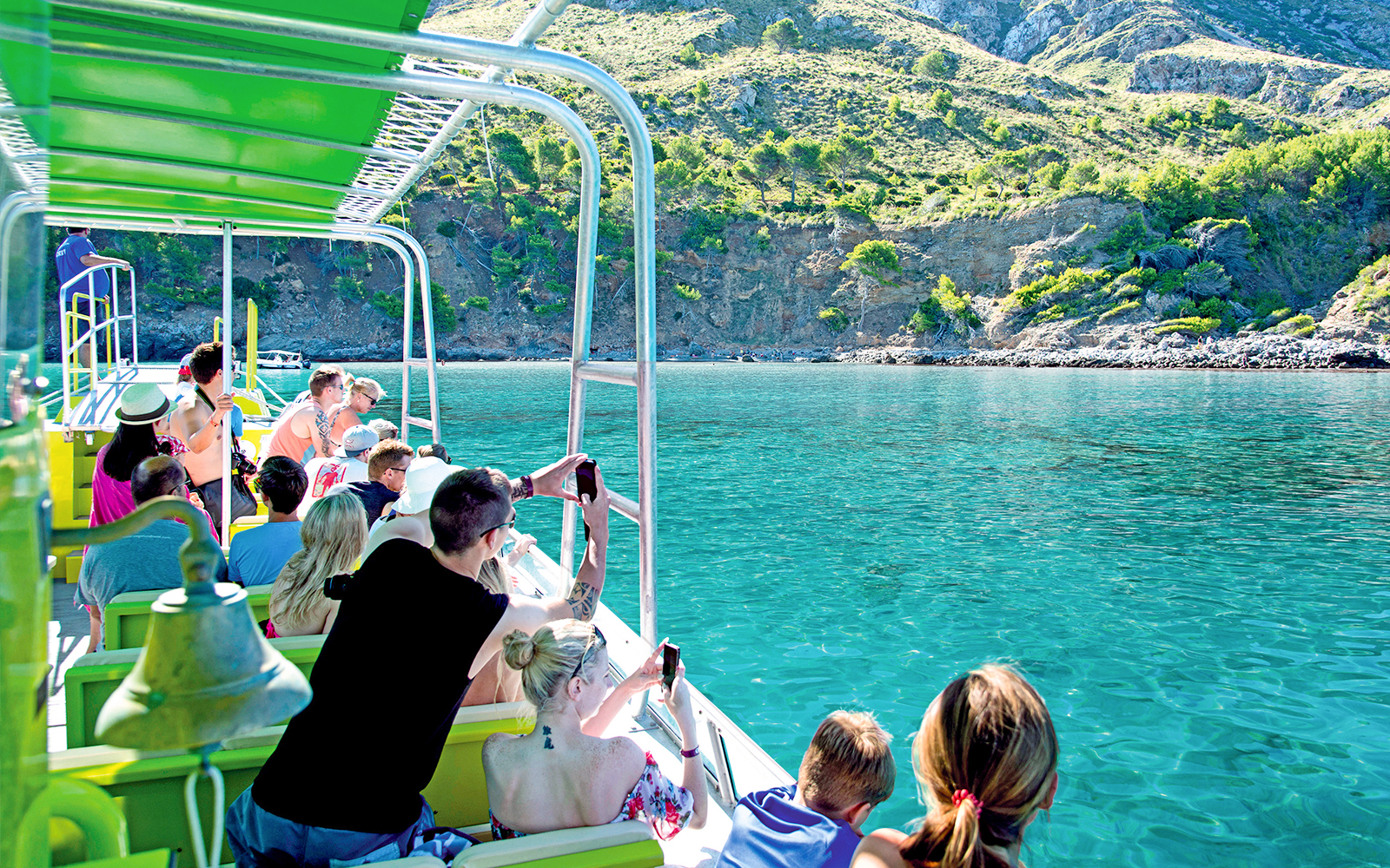 Tourists on a boat enjoying views of Alcudia's coastline and clear waters.