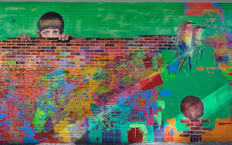 Colorful graffiti mural with a child peeking over a brick wall in Buenos Aires.