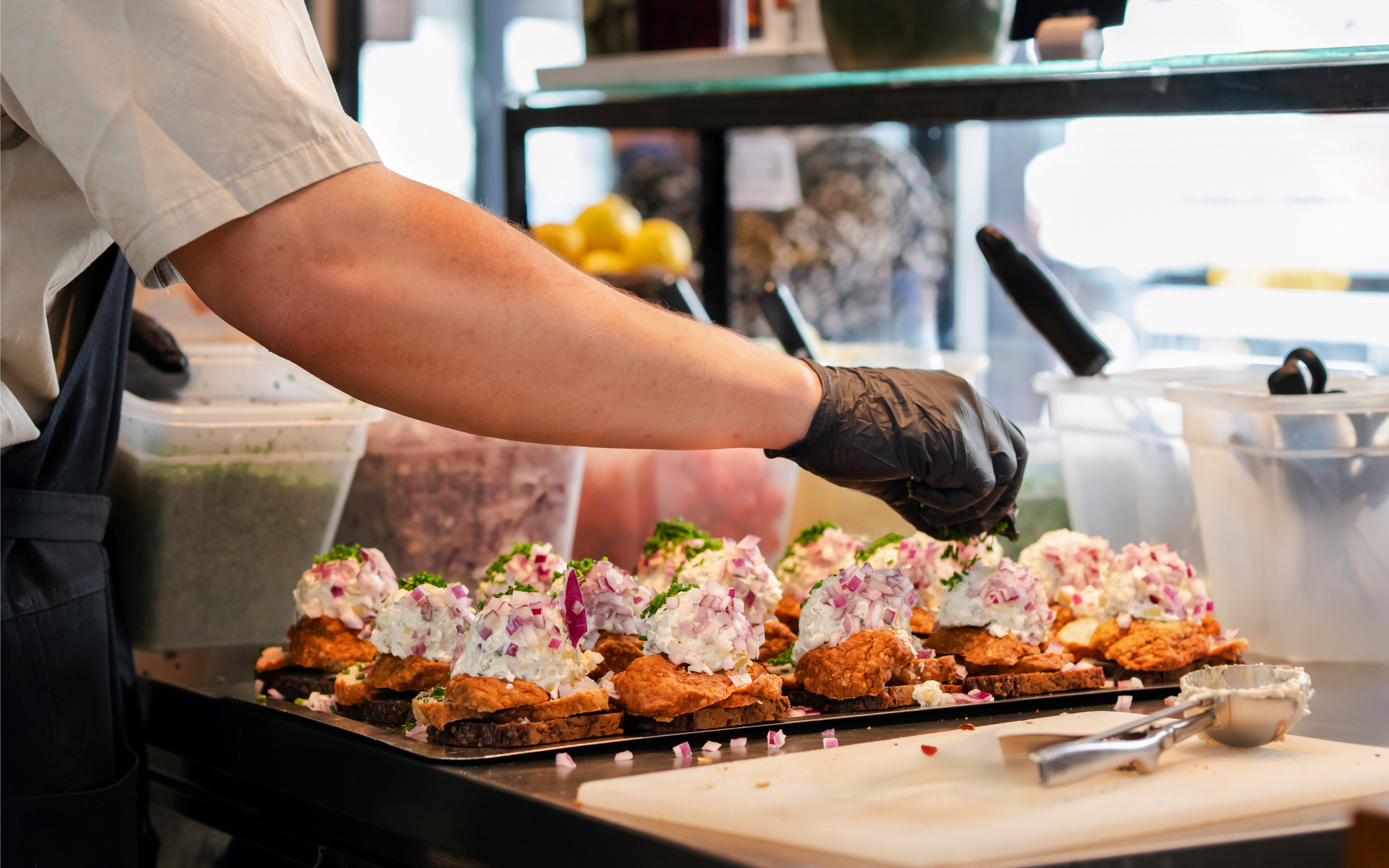 Chef preparing Danish smorrebrod with rye bread and meatballs in a kitchen.