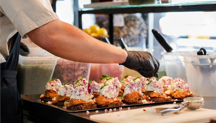 Chef preparing Danish smorrebrod with rye bread and meatballs in a kitchen.