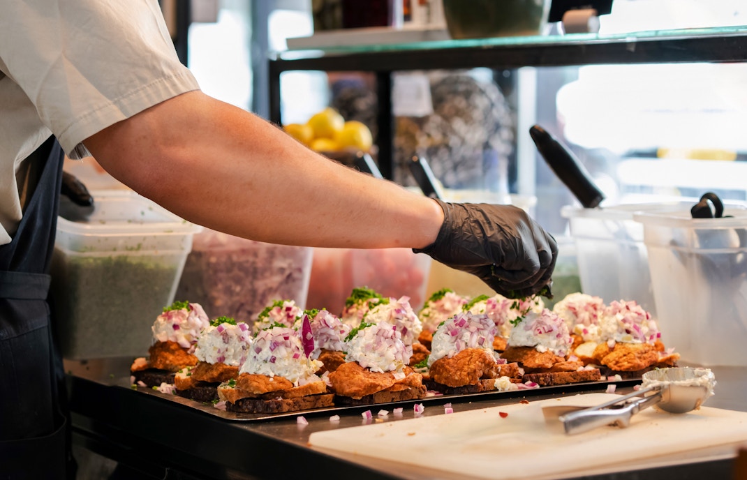 Chef preparing Danish smorrebrod with rye bread and meatballs in a kitchen.
