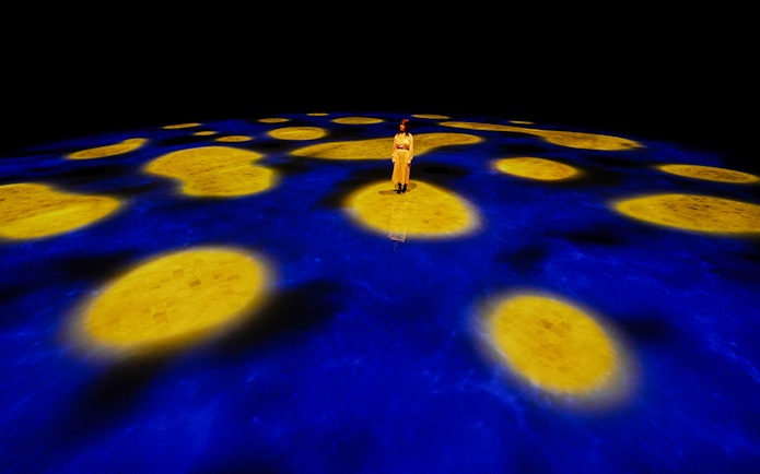 Person standing on illuminated blue and yellow interactive floor at Team Lab Abu Dhabi.