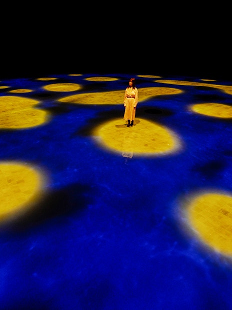 Person standing on illuminated blue and yellow interactive floor at Team Lab Abu Dhabi.