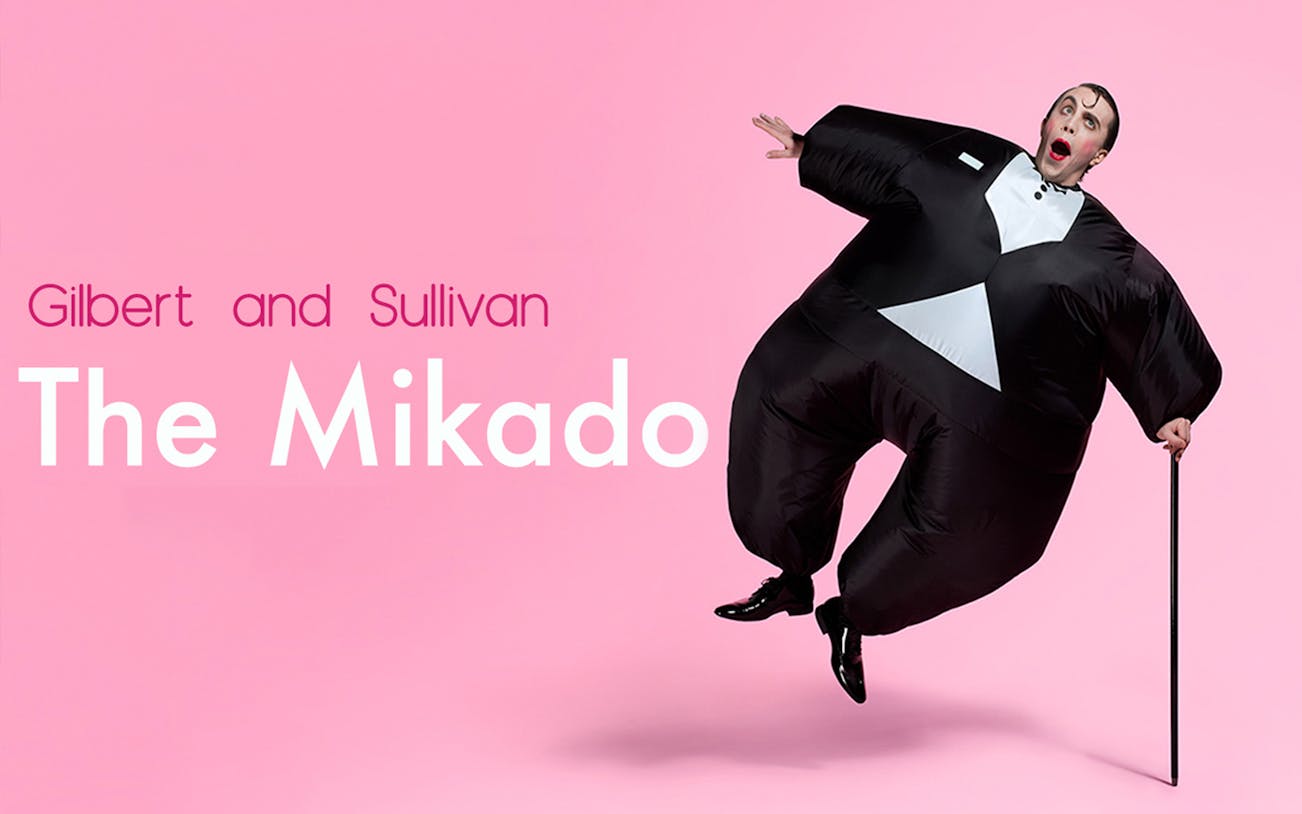 Performer in an inflatable tuxedo costume for The Mikado on a pink background.