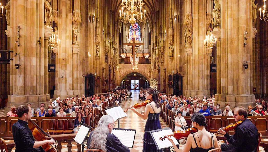 Orchestra performing inside St. Stephen's Cathedral, Vienna, with audience seated.