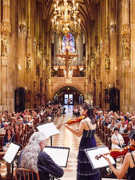 Orchestra performing inside St. Stephen's Cathedral, Vienna, with audience seated.