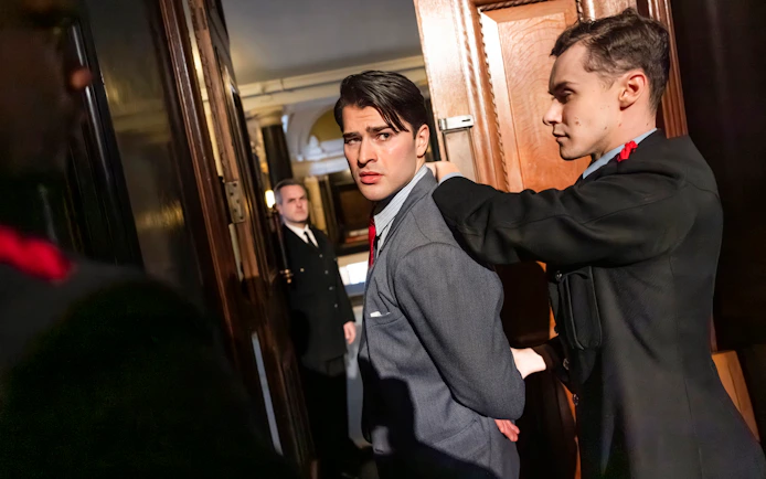 Actor being escorted by guards in a courtroom scene from "Witness for the Prosecution" performance.