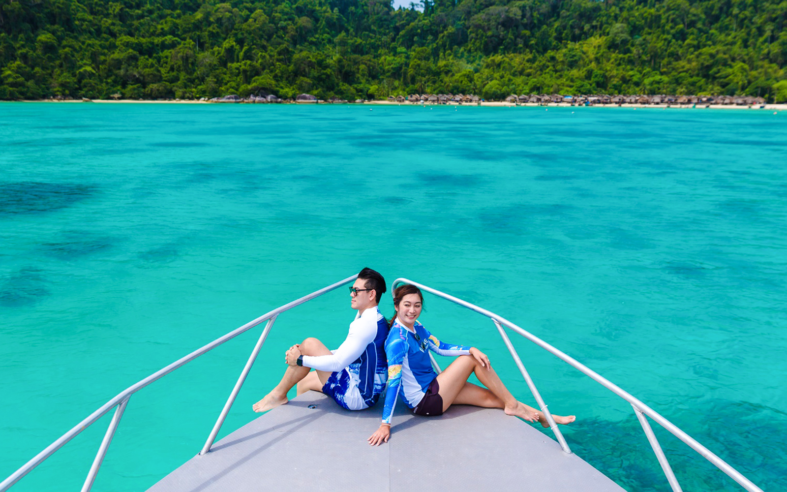 Tourists on a boat heading to Moken village, turquoise sea and lush coastline in view.