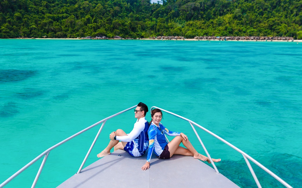 Tourists on a boat heading to Moken village, turquoise sea and lush coastline in view.