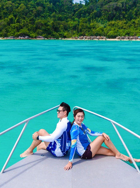 Tourists on a boat heading to Moken village, turquoise sea and lush coastline in view.