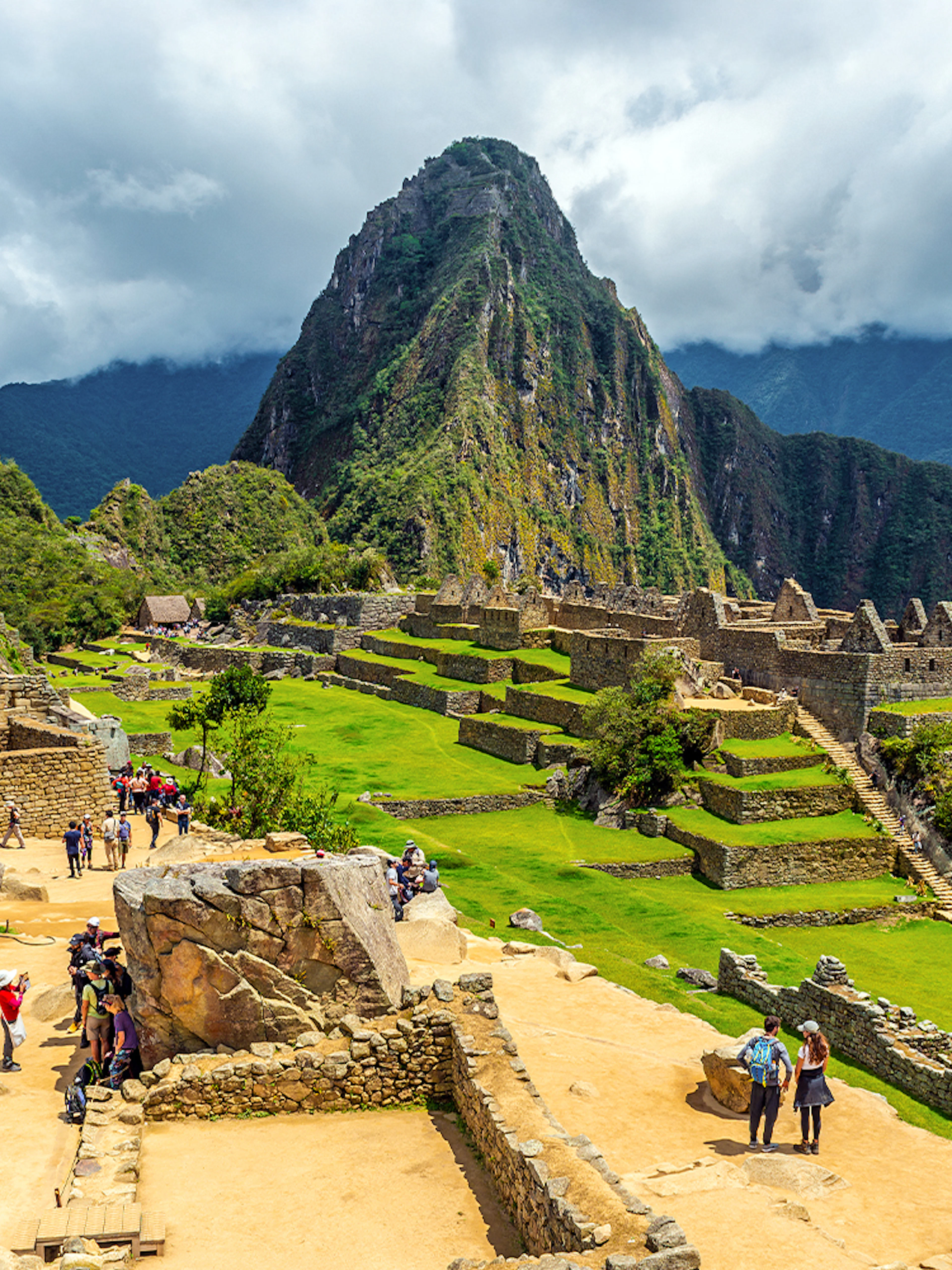 Tourists exploring ancient ruins of Machu Picchu with Huayna Picchu in the background.