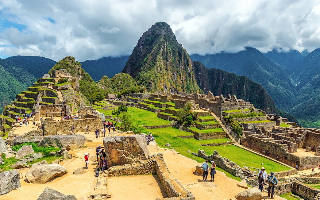 Tourists exploring ancient ruins of Machu Picchu with Huayna Picchu in the background.