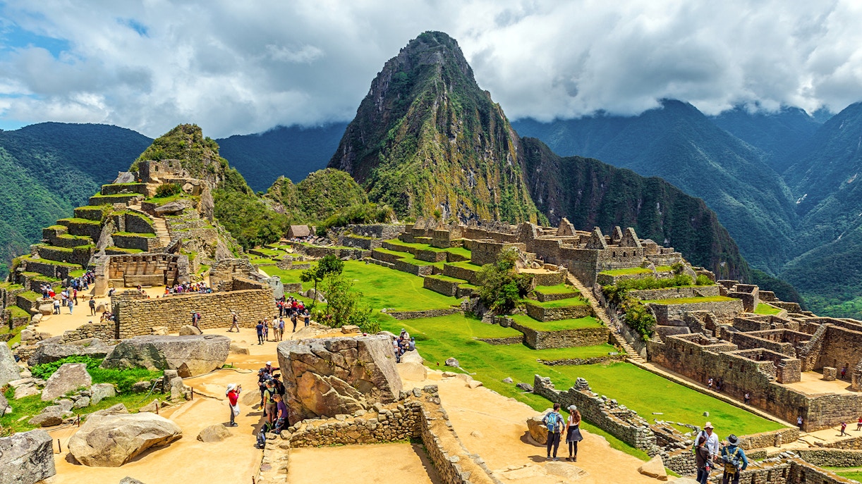 Tourists exploring ancient ruins of Machu Picchu with Huayna Picchu in the background.