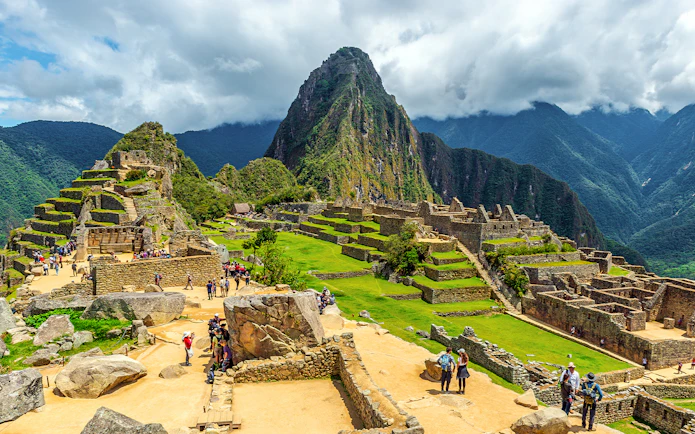 Tourists exploring ancient ruins of Machu Picchu with Huayna Picchu in the background.