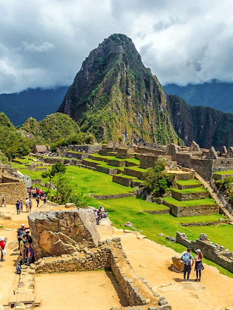 Tourists exploring ancient ruins of Machu Picchu with Huayna Picchu in the background.