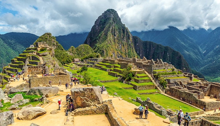 Tourists exploring ancient ruins of Machu Picchu with Huayna Picchu in the background.