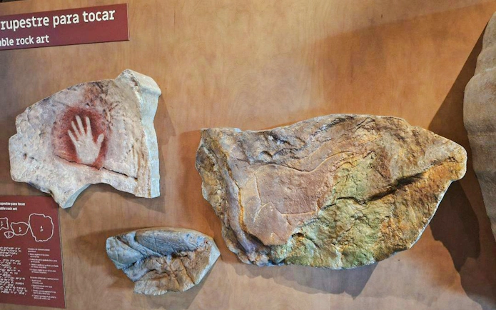 Rock art with hand stencil from El Castillo caves displayed on a wall.